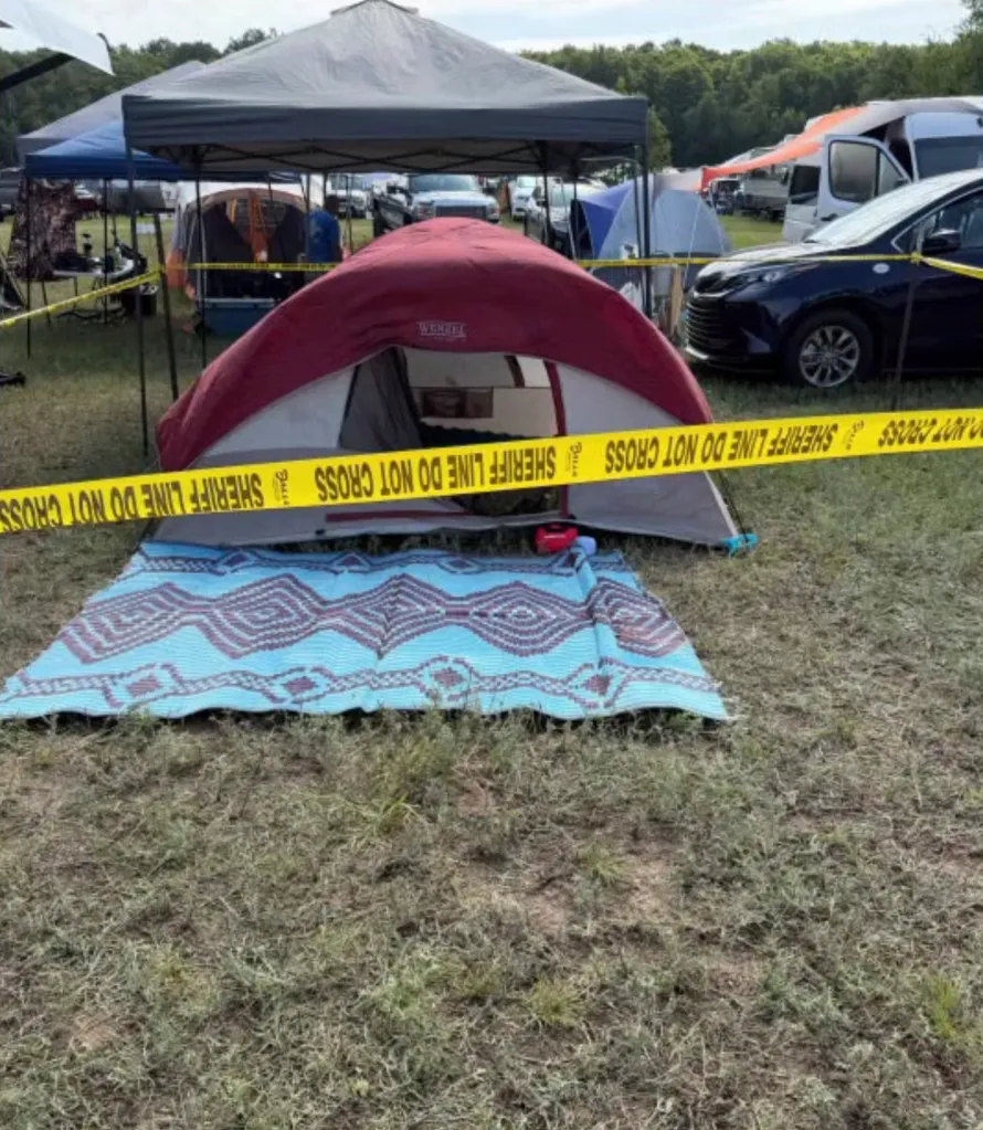 A red and gray tent with a blue mat in front, cordoned off by yellow "SHERIFF LINE DO NOT CROSS" tape.