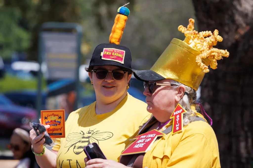 Two women wearing funny hats made of fries and holding a "Los Angeles French Fry Festival" passport.