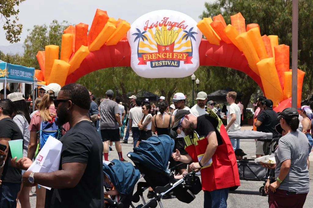 Attendees at the Los Angeles French Fry Festival walk under an inflatable archway decorated like a carton of french fries.