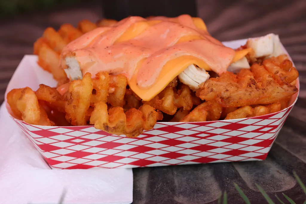A red and white checkered paper container filled with waffle fries topped with melted cheese and a creamy pink sauce.