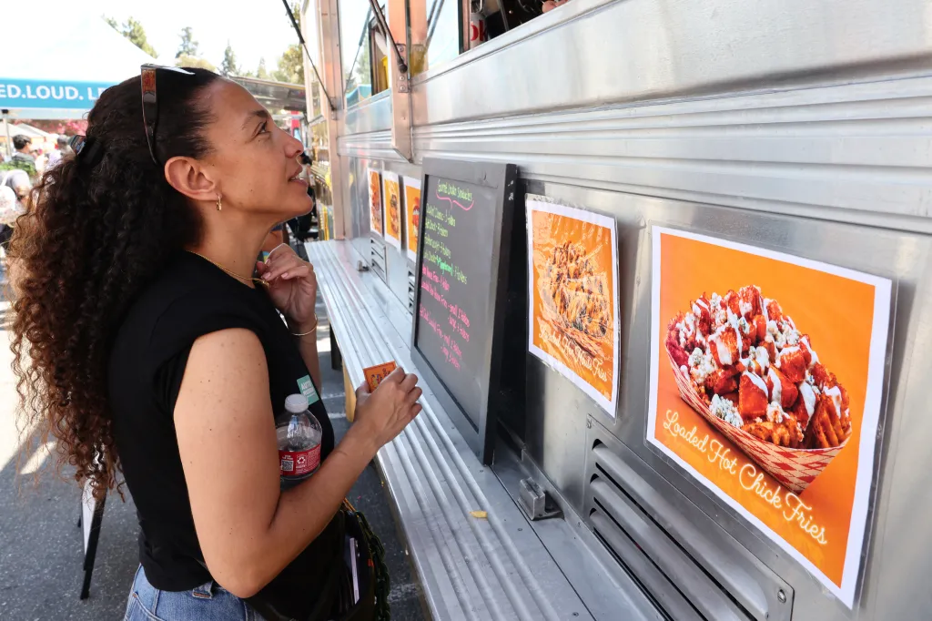 A woman looking at the menu and pictures of loaded fries on a food truck at the Los Angeles French Fry Festival.