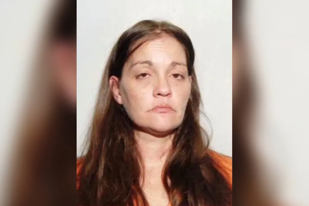 Mugshot of a woman with long brown hair, wearing an orange shirt.