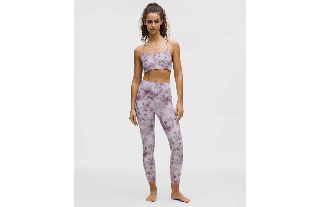 A woman wearing a pair of leggings in a purple and white print, and a matching sports bra.