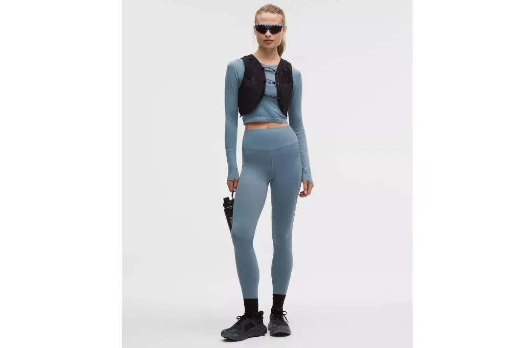 A woman in light blue leggings, a matching top and a black vest.