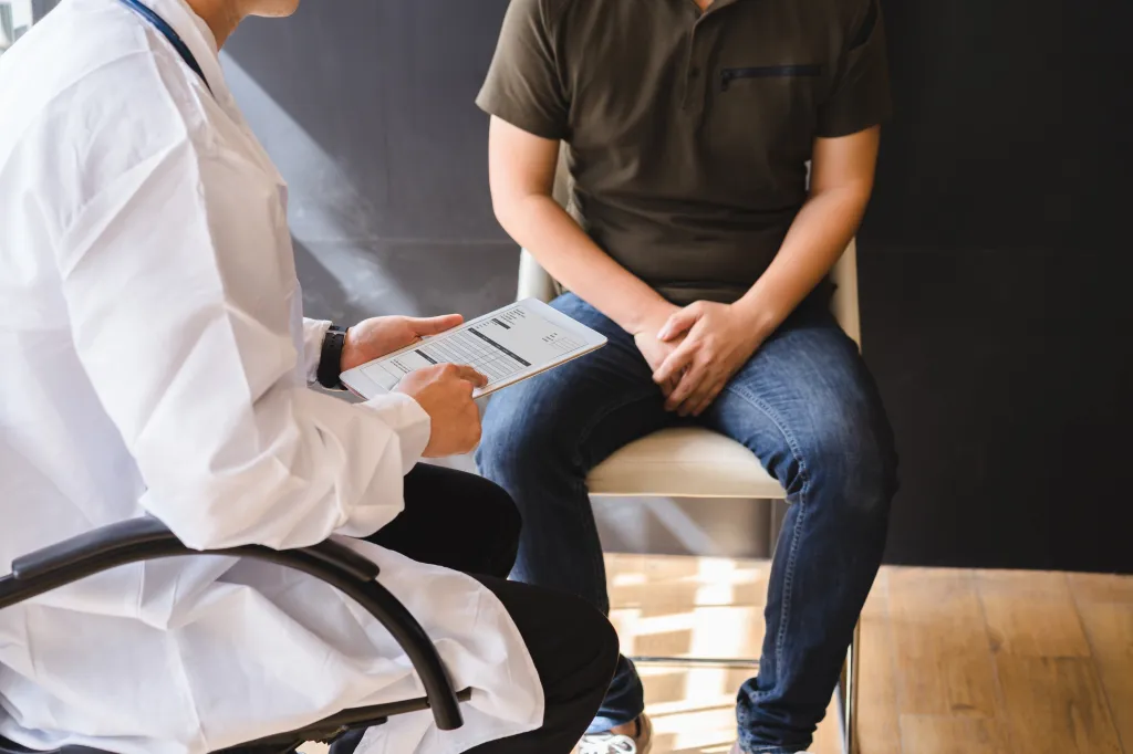 A doctor discusses a report on a tablet with a male patient sitting across from them, highlighting discussions about testicular and prostate cancer.