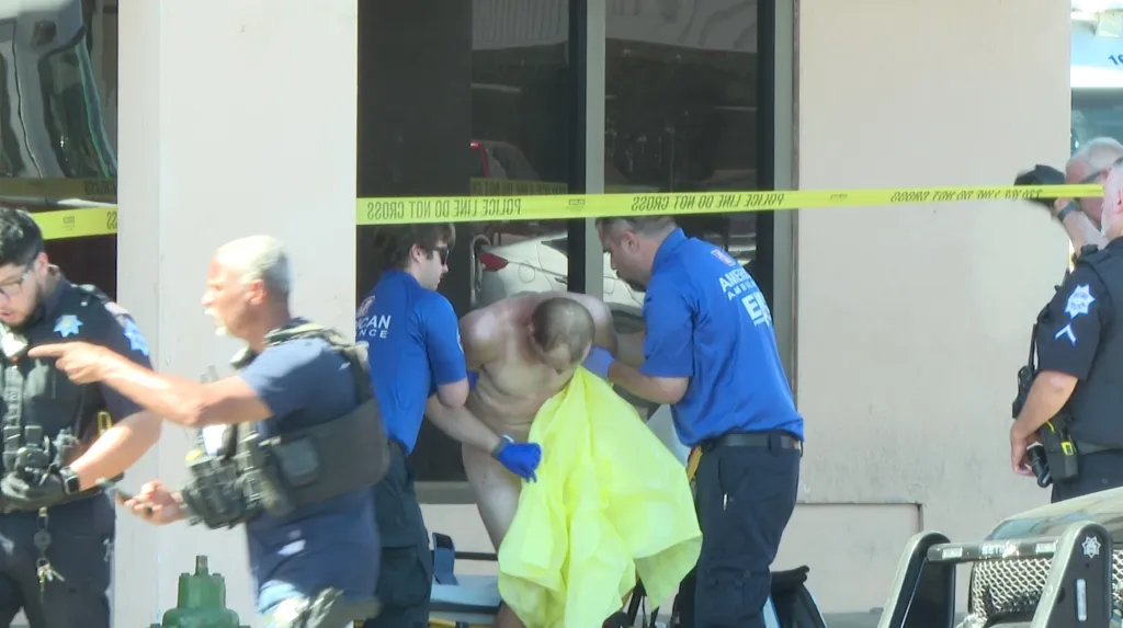 Police and emergency personnel attending to a partially covered man in a crime scene.