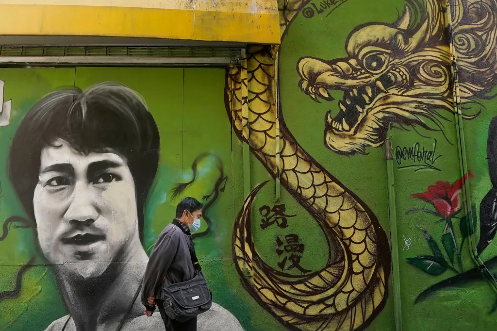 A man in a face mask walks past a mural of Bruce Lee and a dragon.