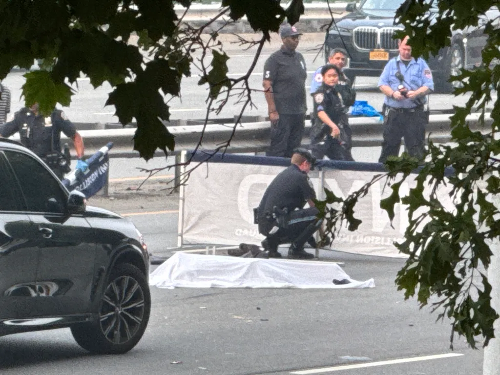 Law enforcement officers on a highway, with a body covered by a white sheet.
