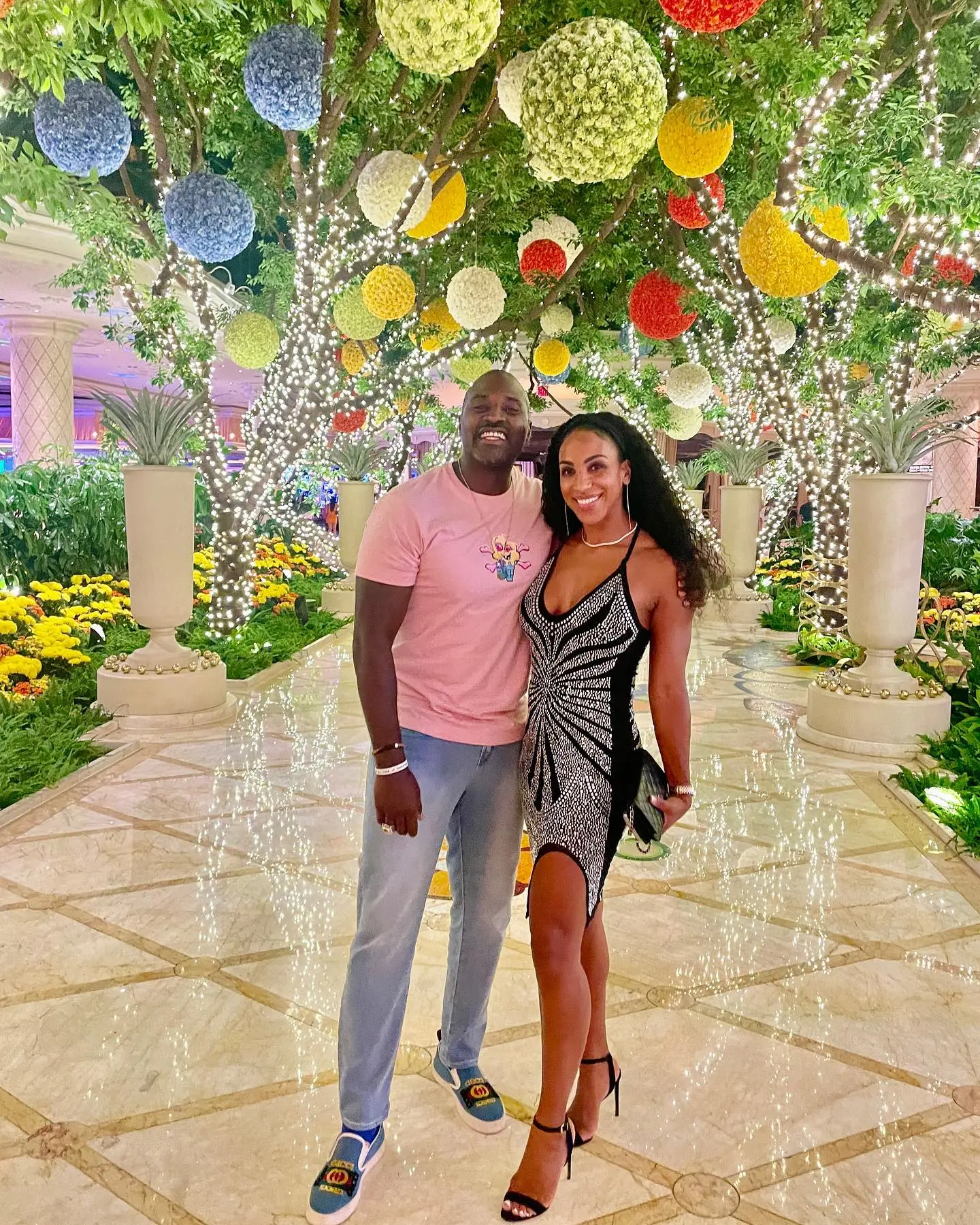 Marcellus and Annemarie Wiley posing in a garden with brightly lit trees and colorful floral decorations.