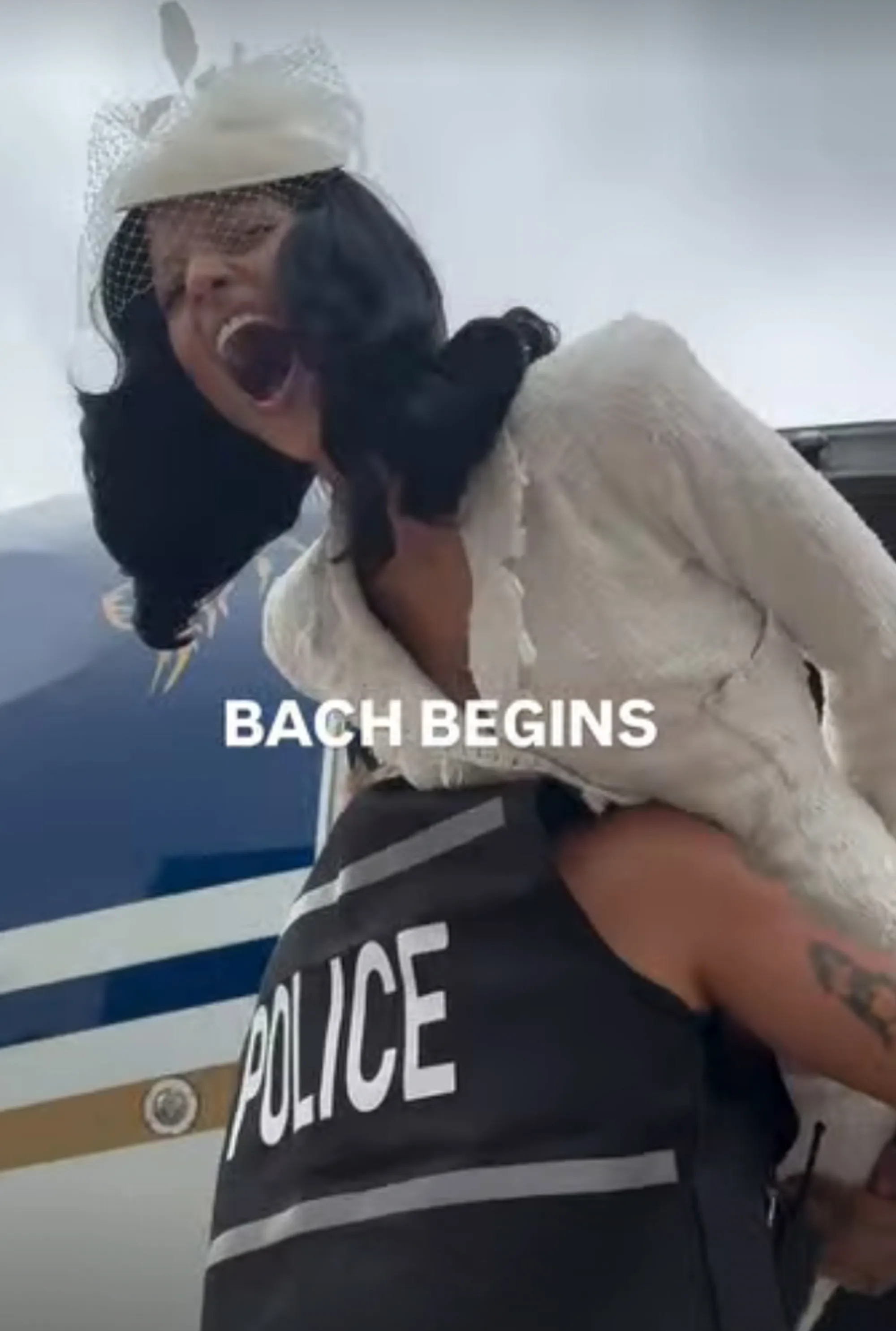 Gabriette being carried by someone in a "POLICE" vest as she screams in excitement, with the text "BACH BEGINS" overlayed.