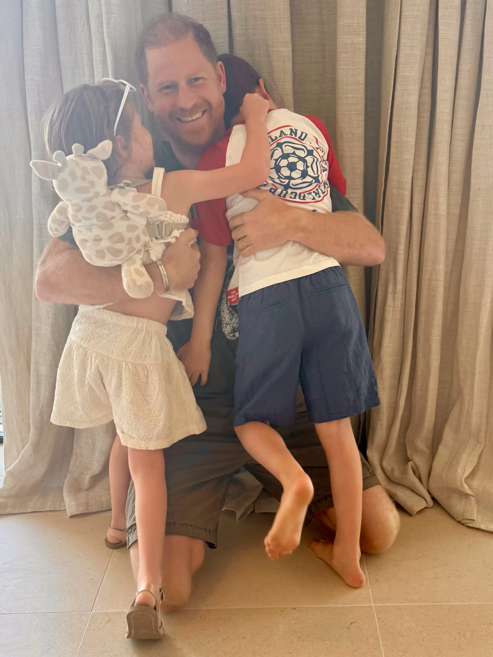 Prince Harry smiling while embracing his two young children.