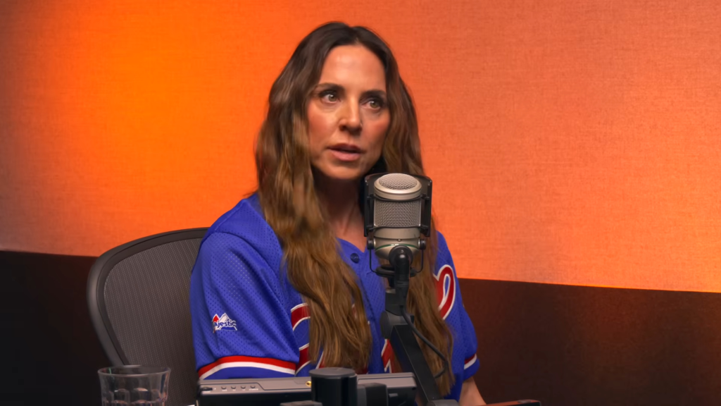 Mel C wearing a blue sports jersey and speaking into a microphone.