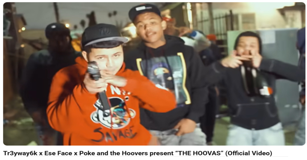 Members of the Hoover Gang in a music video, with one man pointing a gun at the camera and another holding a bottle.