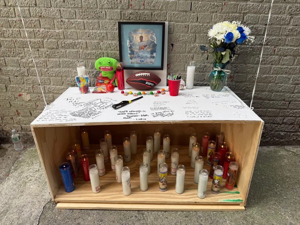 A memorial for Jacob Freytes, featuring a framed photo, candles, flowers, and handwritten messages on a wooden box.