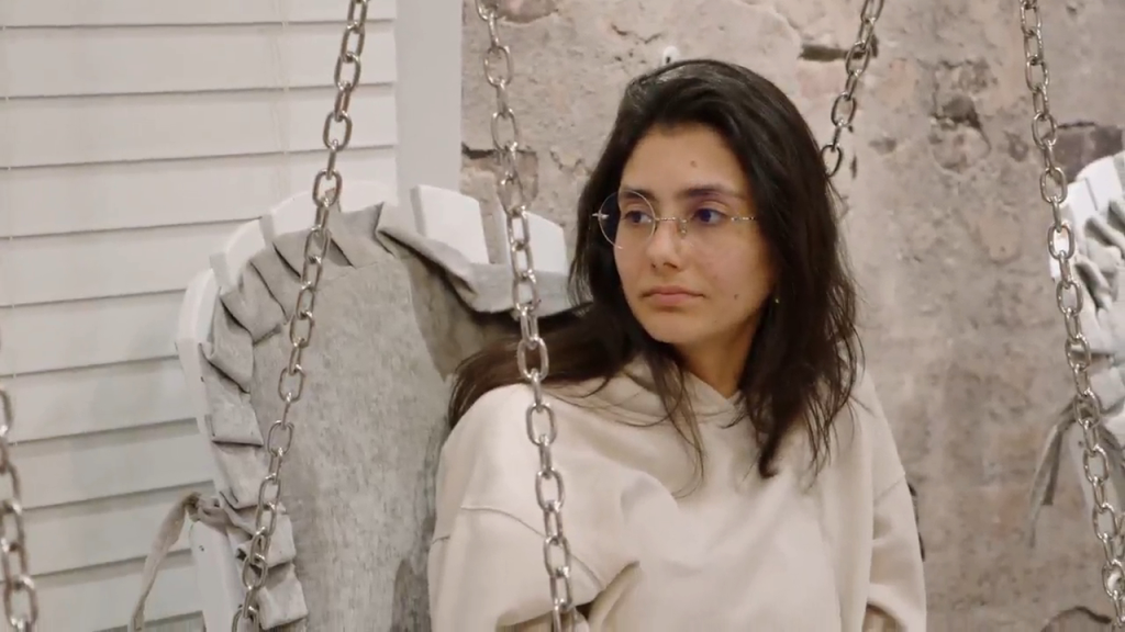 Mido sitting on a swing chair with a neutral expression.