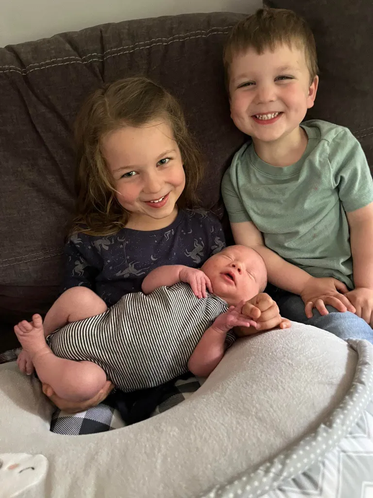 Three young children, a girl, a boy, and a baby, sit together on a sofa.