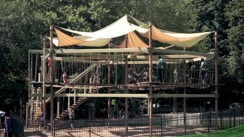 People on a rope course with tan and white sun shades overhead.