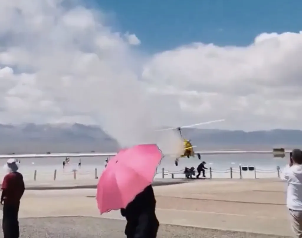 A yellow helicopter crash-lands near two people on a salt lake shore as others watch.