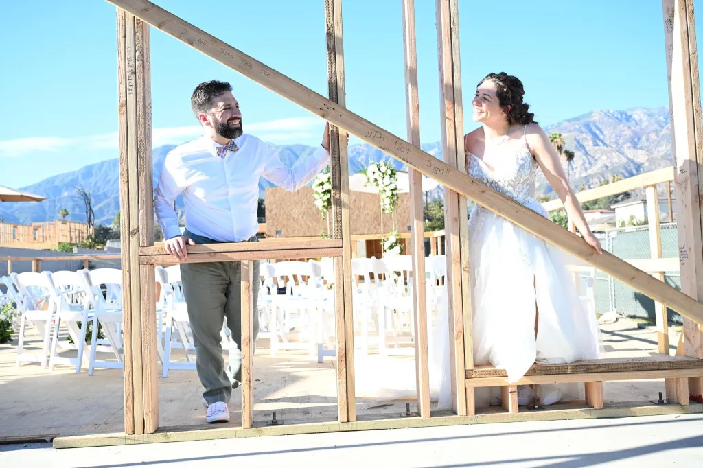 Morgan Soloway and Kenny Rotter, a newlywed couple, walk hand-in-hand through the wooden frame of their rebuilt home.