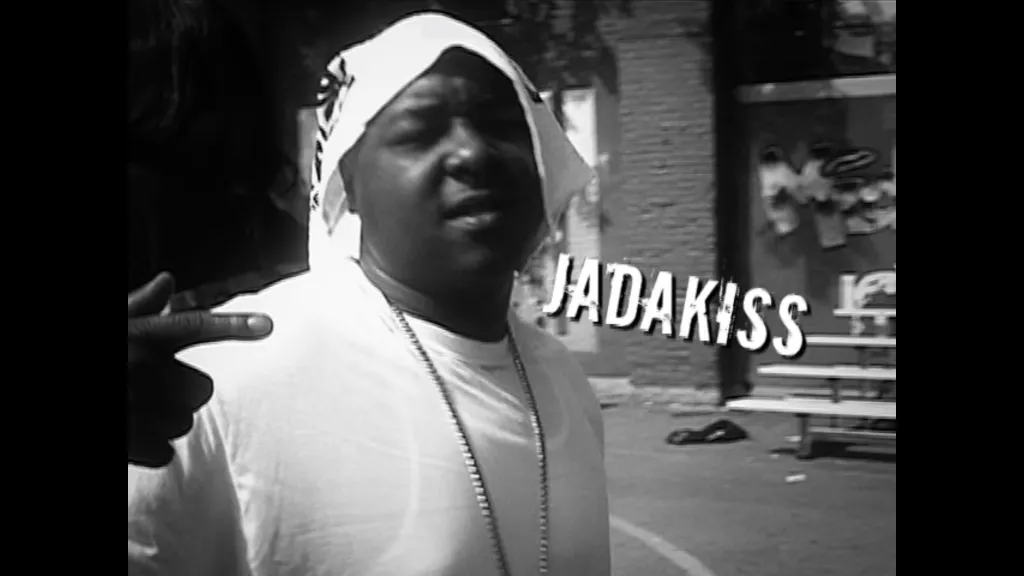 Jadakiss, a Black man in a durag and white t-shirt, stands next to "JADAKISS" in large white lettering.