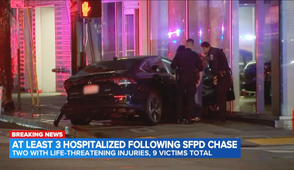 Police officers investigating a car crash with a car pulled over on the sidewalk, with a "BREAKING NEWS" banner at the bottom stating "AT LEAST 3 HOSPITALIZED FOLLOWING SFPD CHASE TWO WITH LIFE-THREATENING INJURIES, 9 VICTIMS TOTAL".