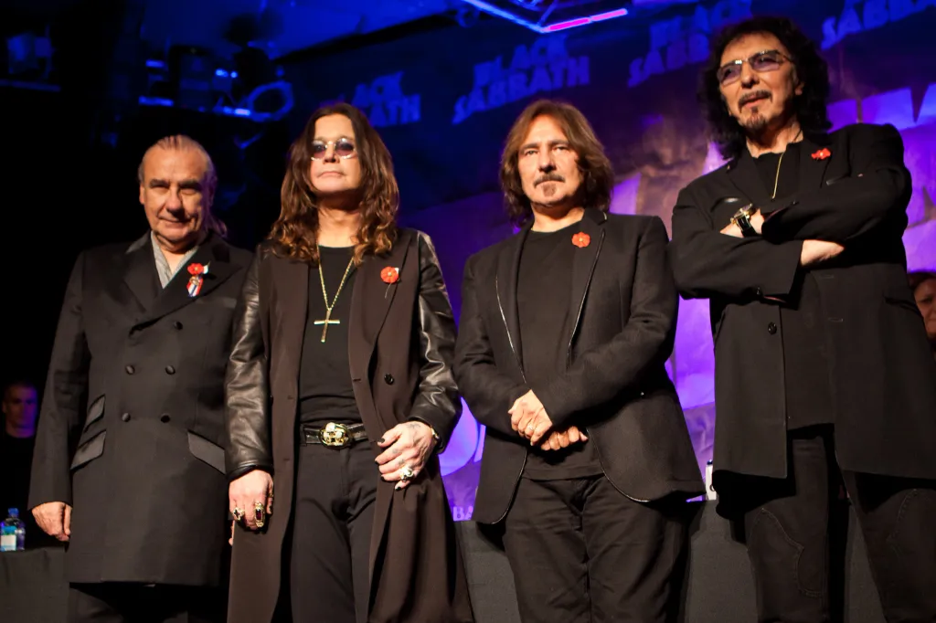 Black Sabbath musicians Bill Ward, Ozzy Osbourne, Geezer Butler, and Tony Iommi standing on stage.