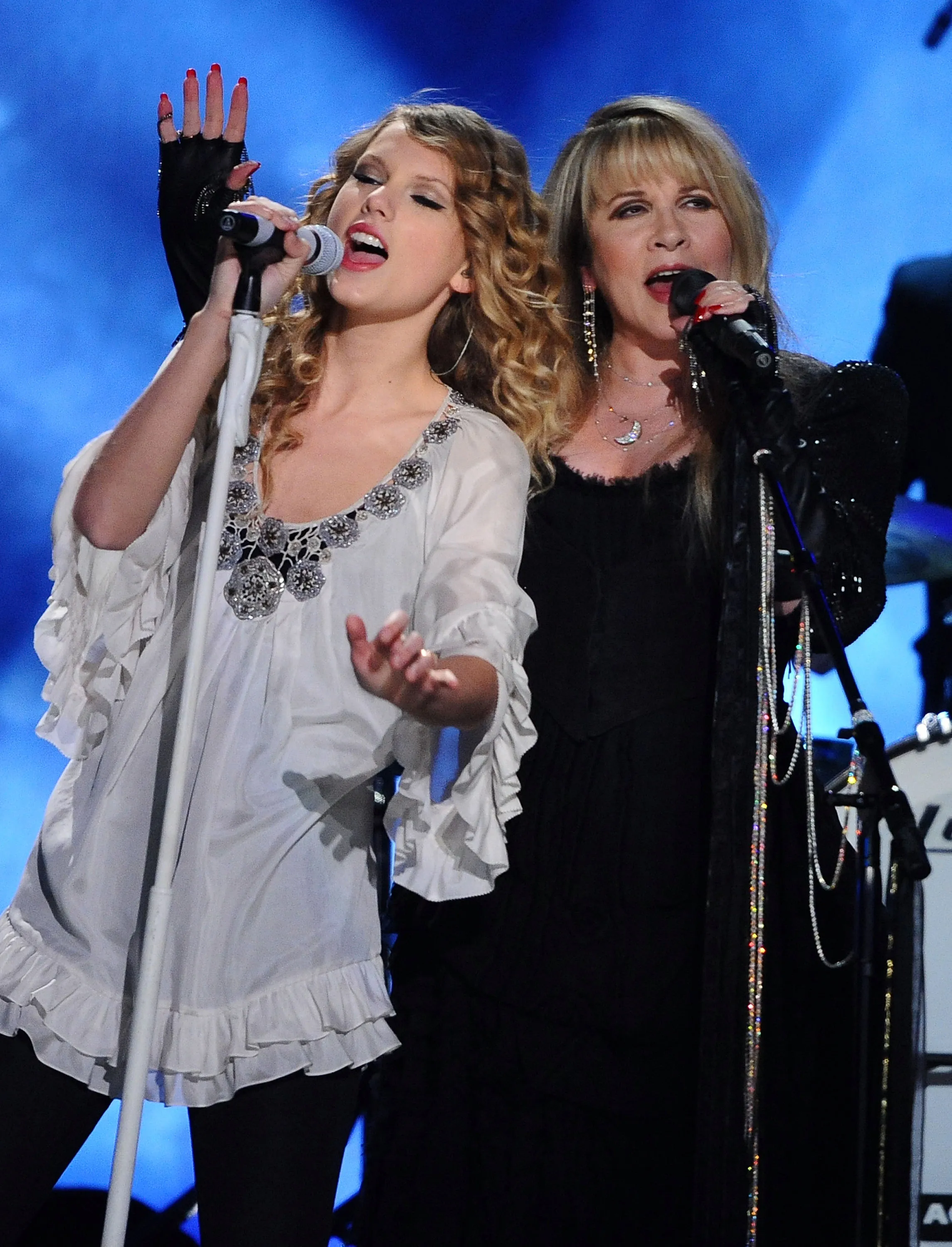 Taylor Swift and Stevie Nicks singing into microphones on stage.