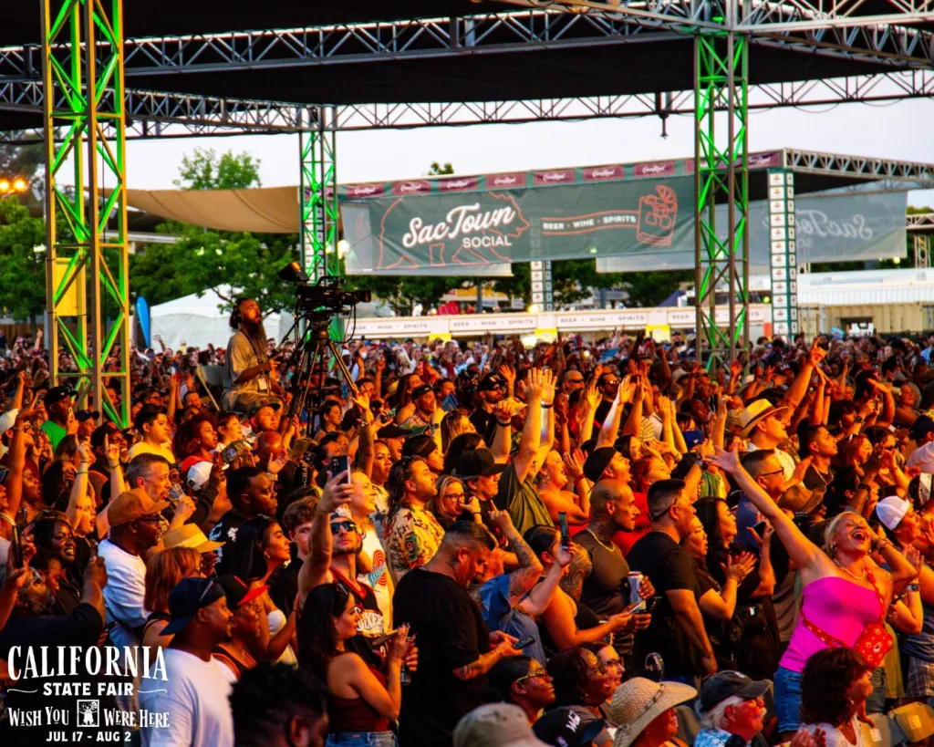 Crowd of people at the California State Fair Sac Town Social concert venue with their hands raised.