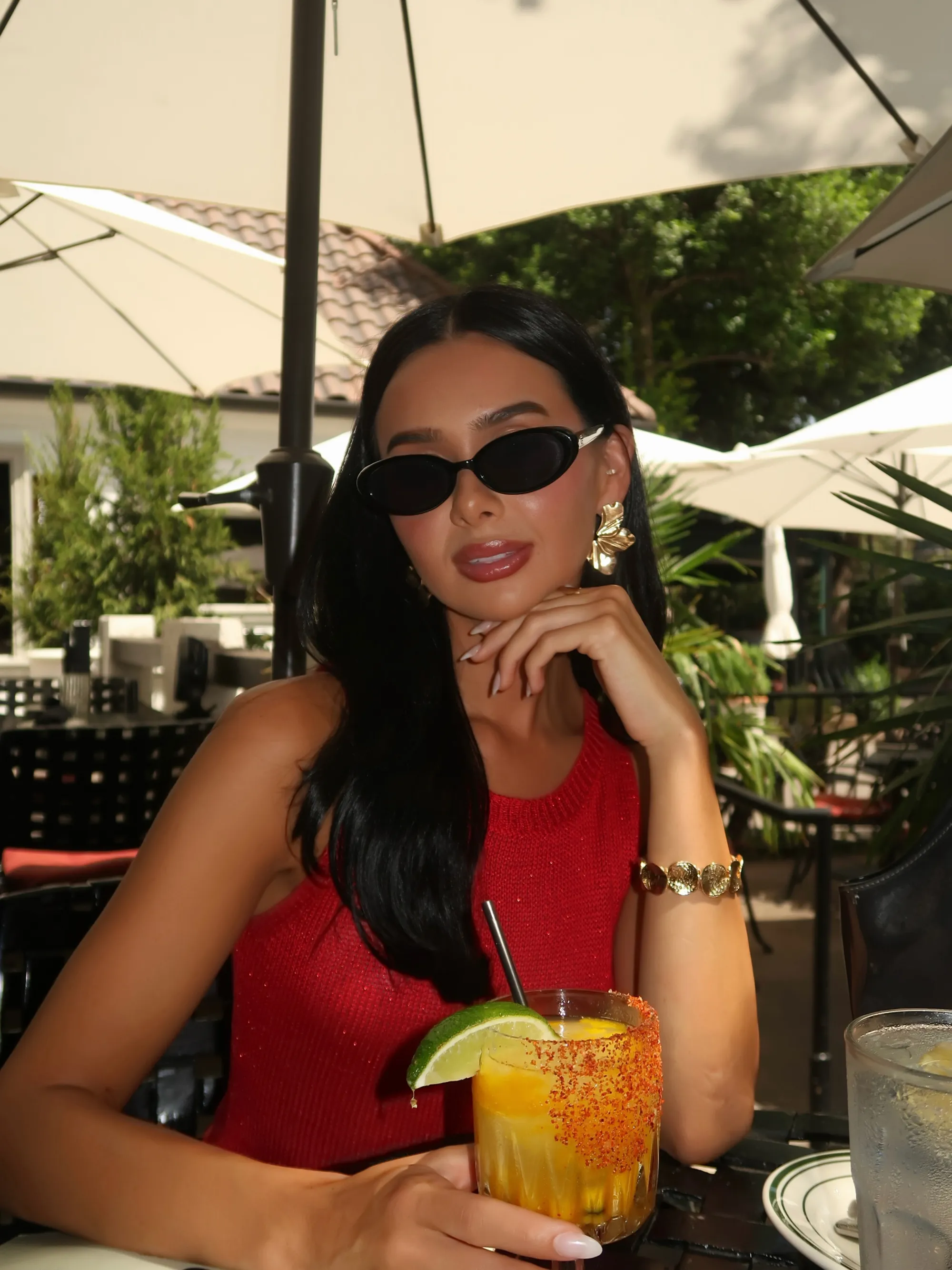 Hayley Hendrich sitting at a table with a drink, wearing sunglasses and a red top.