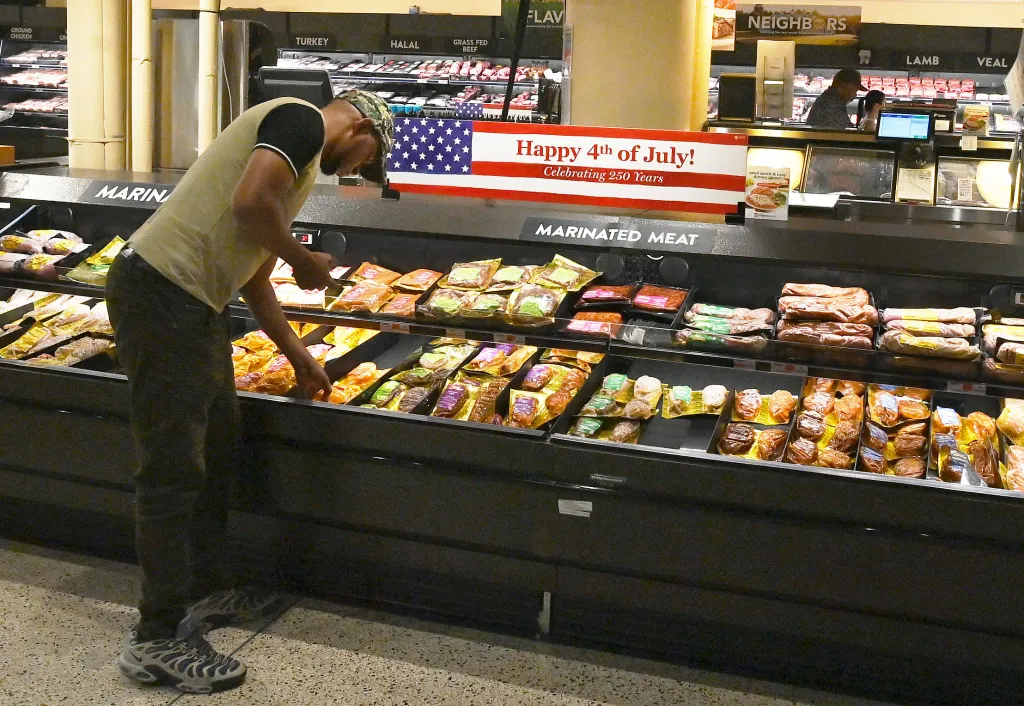 A shopper at Wegmans .looks at packaged marinated meats in a grocery store with a "Happy 4th of July!" sign overhead.
