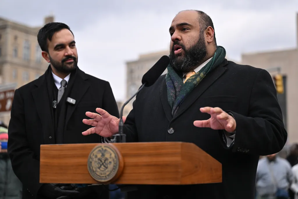Mayor Zorhan Mamdani speaking at a press conference, with Ali Najmi standing behind him.
