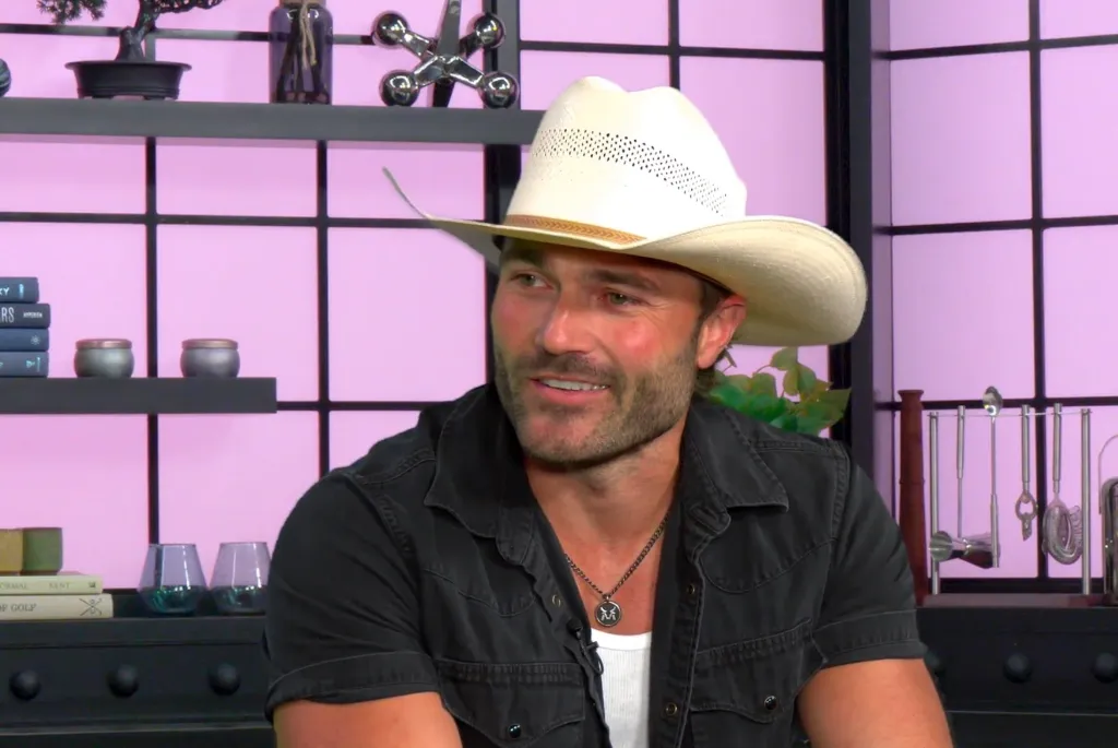A man in a white cowboy hat and black shirt looks right, smiling.