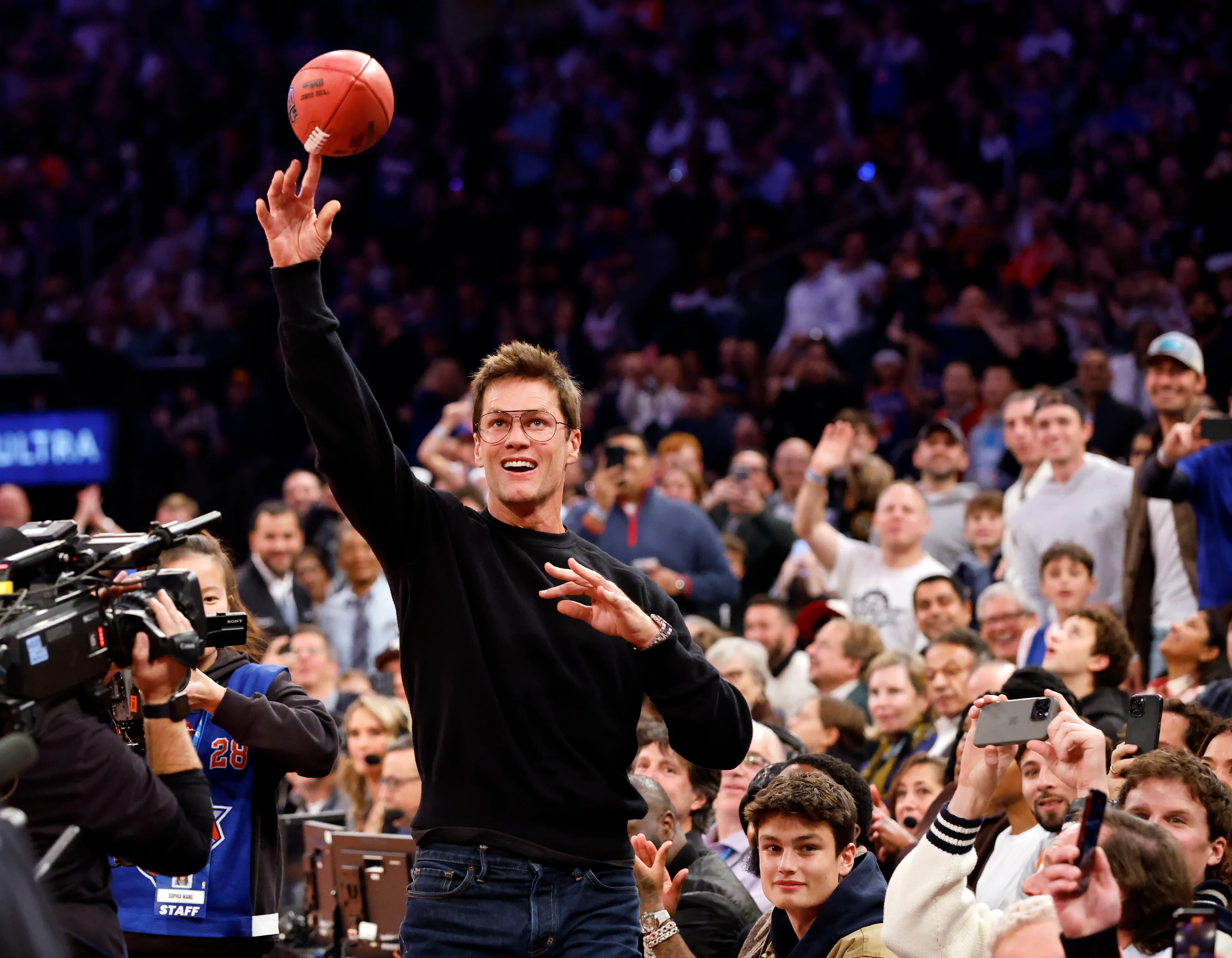 Tom Brady spinning a football on his finger at a basketball game.
