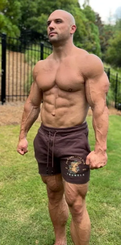 Bodybuilder Nick Trigili posing shirtless in a garden.