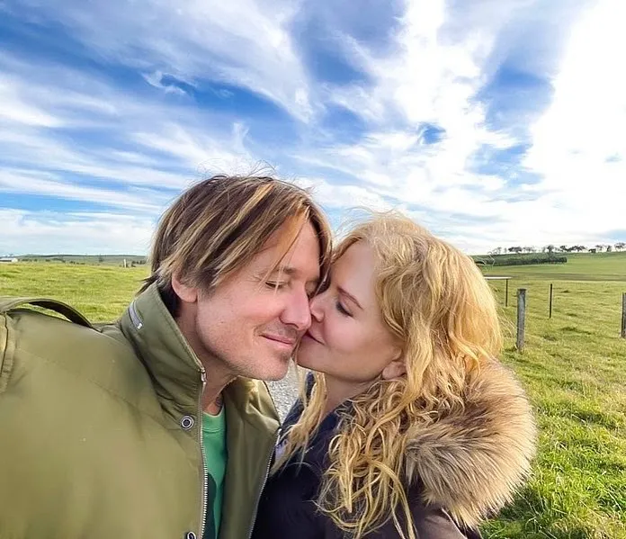 Nicole Kidman and Keith Urban kissing outdoors under a blue sky.