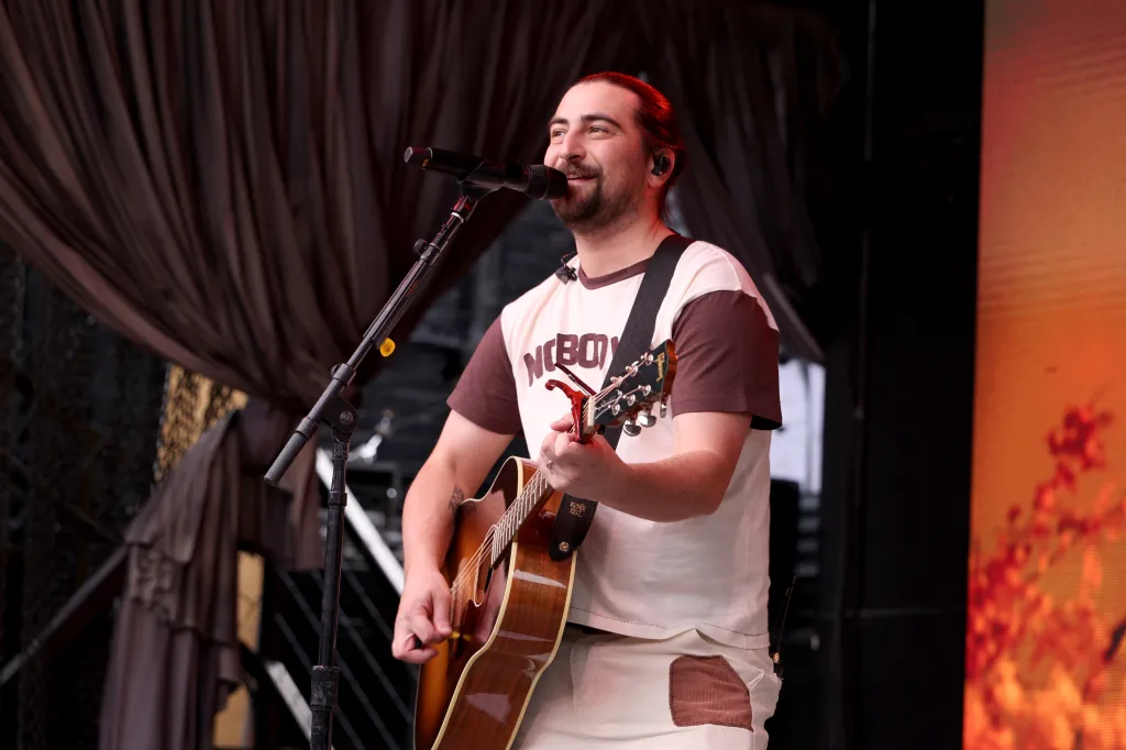 Noah Kahan performing onstage with an acoustic guitar.