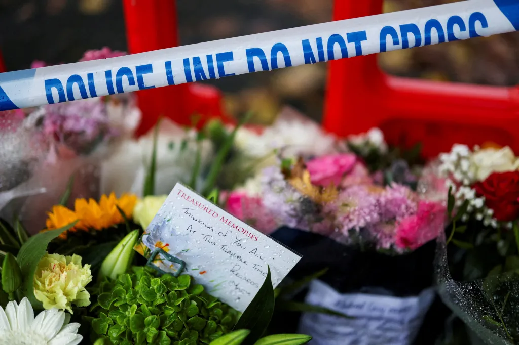 Police tape above floral tributes and a handwritten note with a message of sympathy.