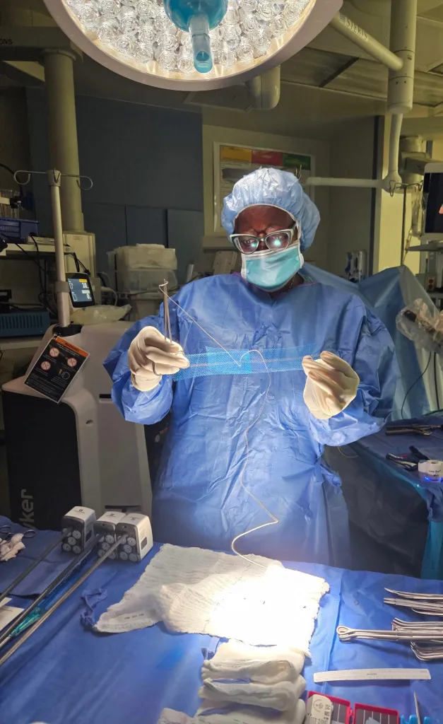 Nyarai Mushonga, M.D., a double board-certified urogynecologist, holds up a surgical mesh in an operating room.