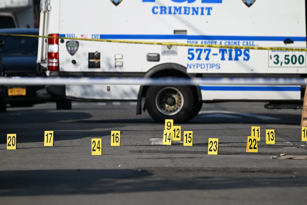 Evidence markers on the ground in front of an NYPD Crime Unit vehicle, with crime scene tape visible.