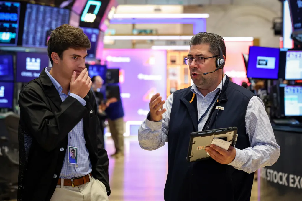 Two traders on the New York Stock Exchange floor, one in a headset holding a tablet, the other with hand to chin.
