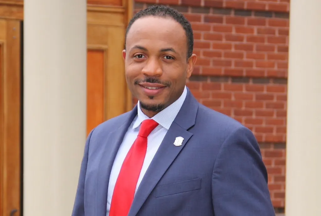 Jestin Johnson wearing a suit and red tie, smiling slightly.