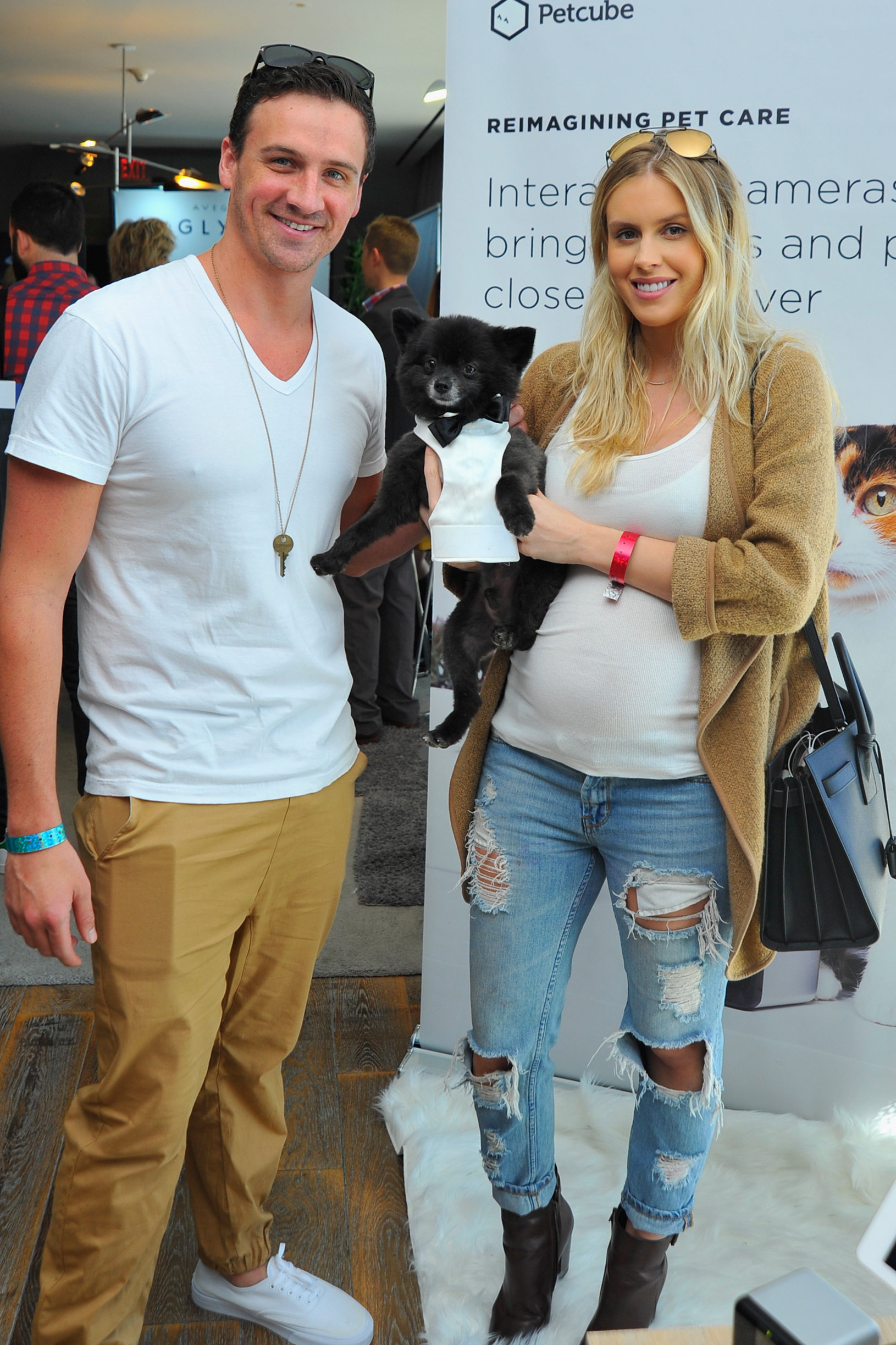 Olympian Ryan Lochte and model Kayla Rae Reid, who is pregnant, hold a small black dog in a tuxedo.