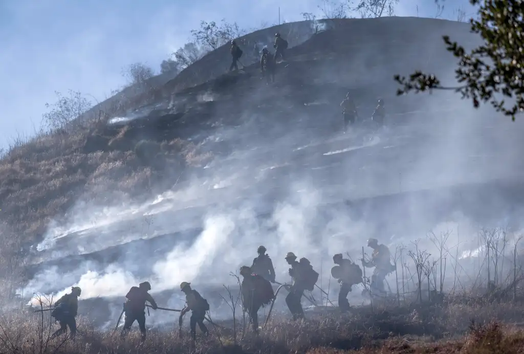 Firefighters battling the Narrow fire in Ladera Ranch, extinguishing flames and embers on a dry, grassy hillside.