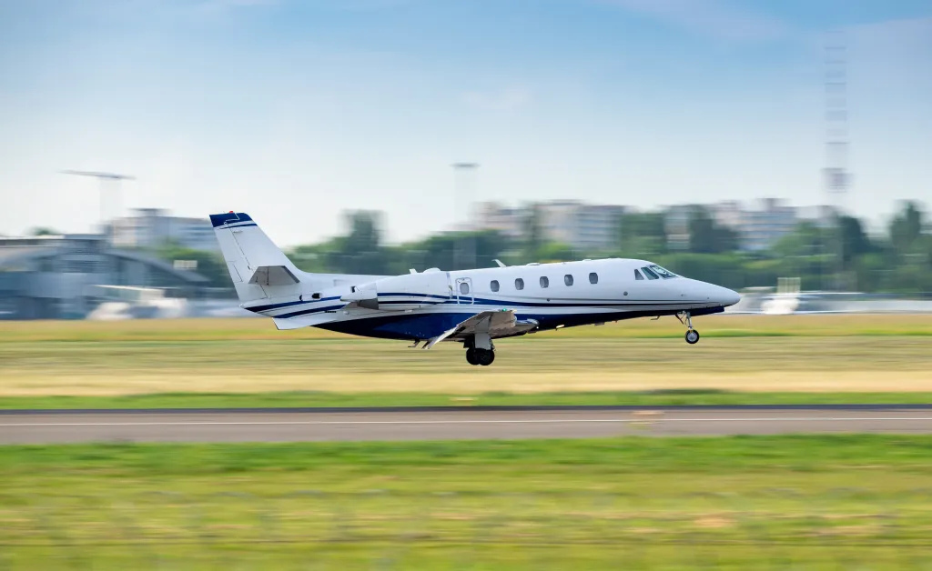 A white and blue business jet landing on an airport runway with a blurry background.