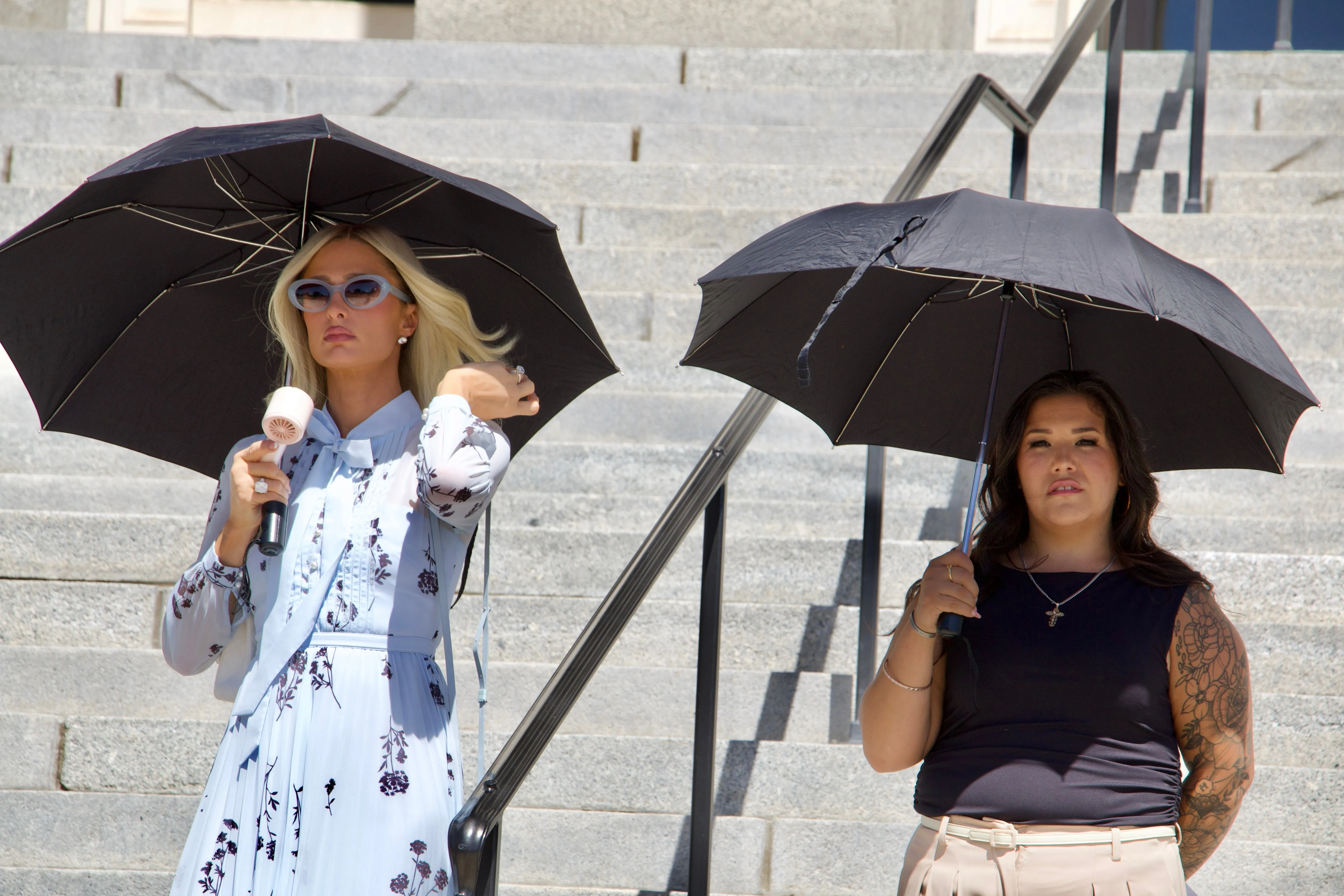 Paris Hilton and Aleah Corona holding umbrellas during a news conference.