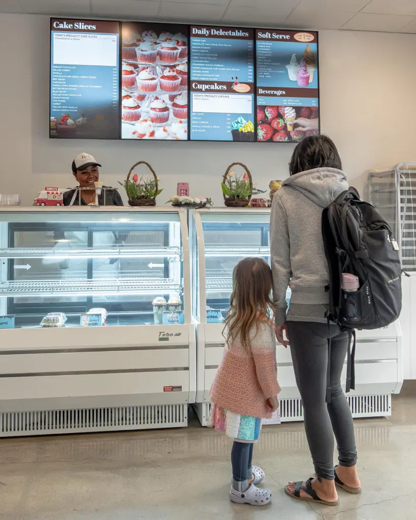 A customer and child looking at empty display cases and a menu board at Sweet Red Peach Bakery.