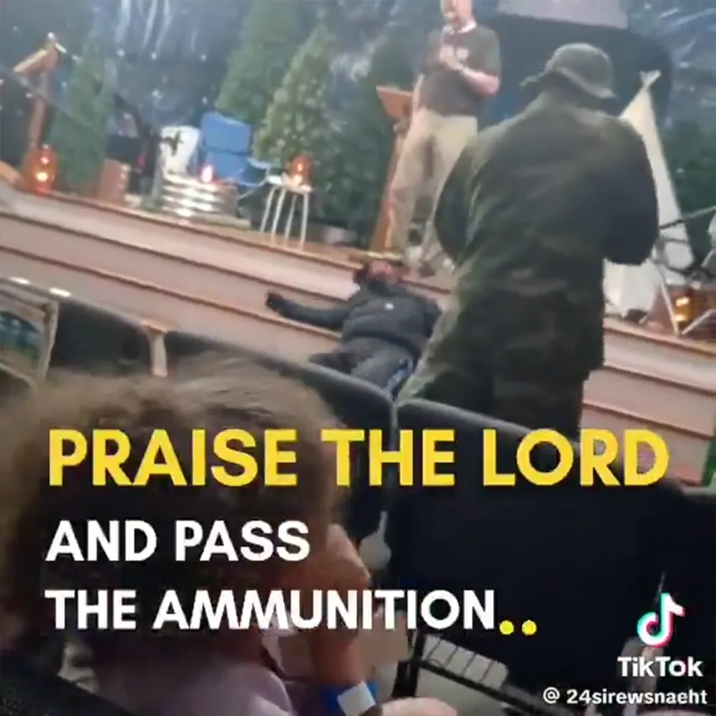 A man in military fatigues stands over another person in black clothing lying on the floor in a church, with "PRAISE THE LORD AND PASS THE AMMUNITION.." superimposed over the image.