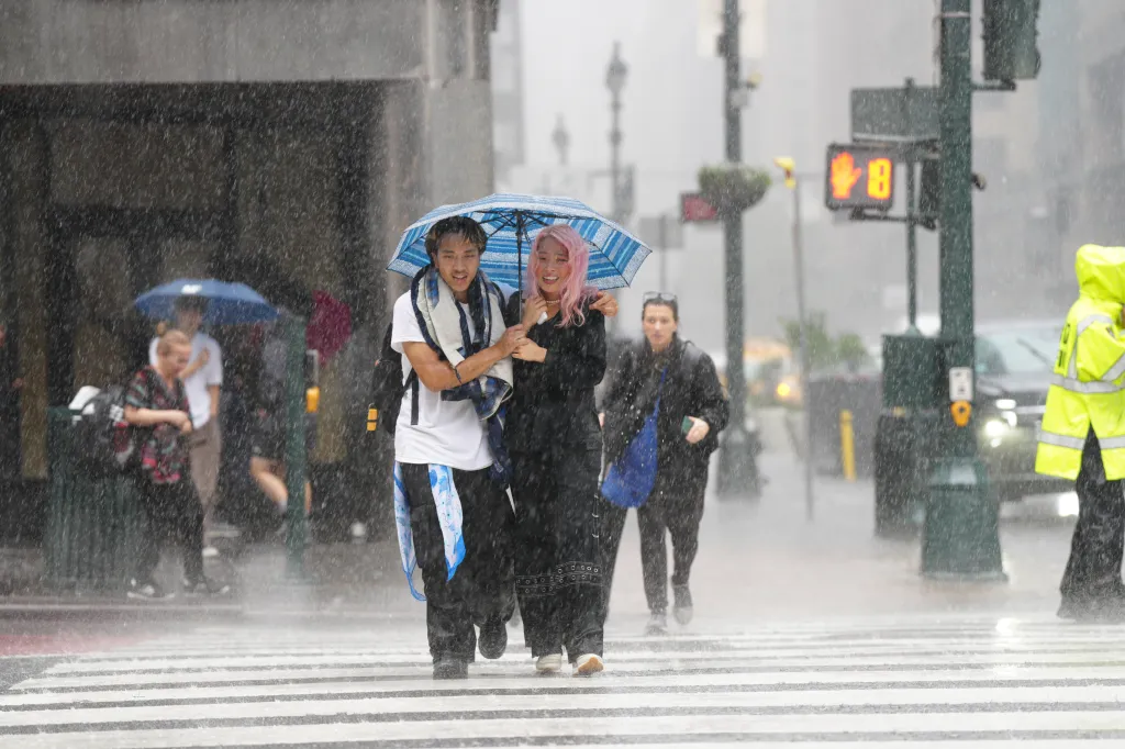 Pedestrians, including a couple sharing a blue and white striped umbrella, walk through heavy rain in Manhattan.