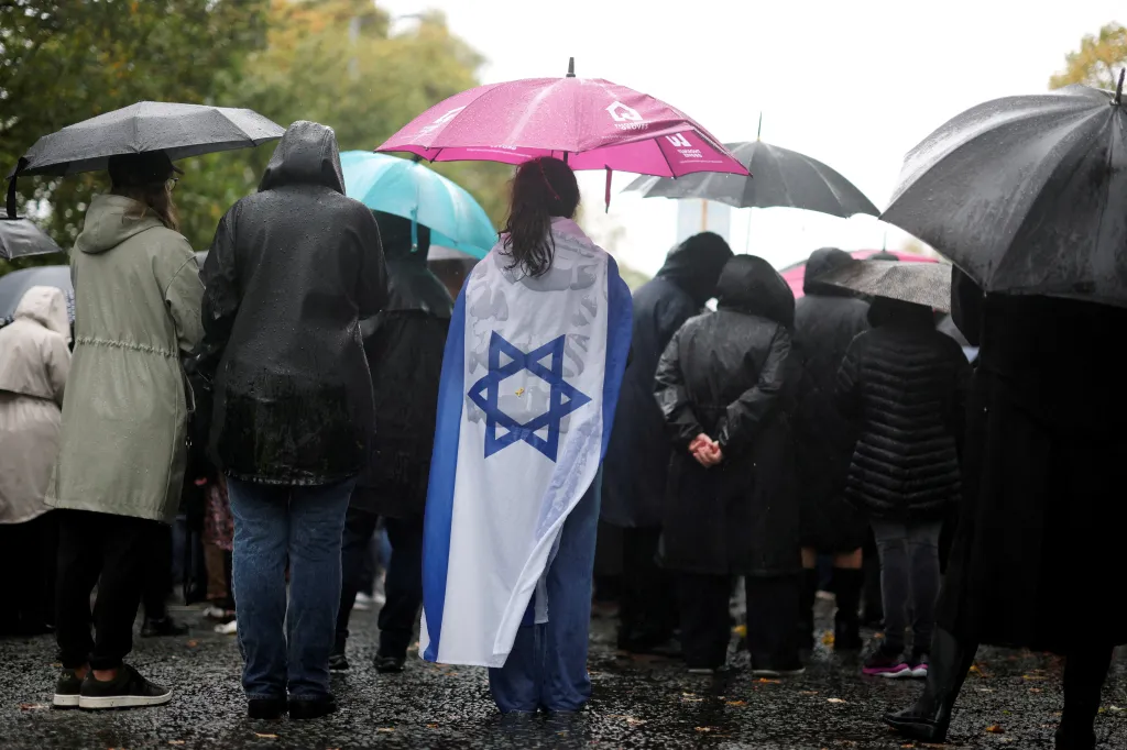 A person in the foreground wears an Israeli flag as a cape during a vigil.