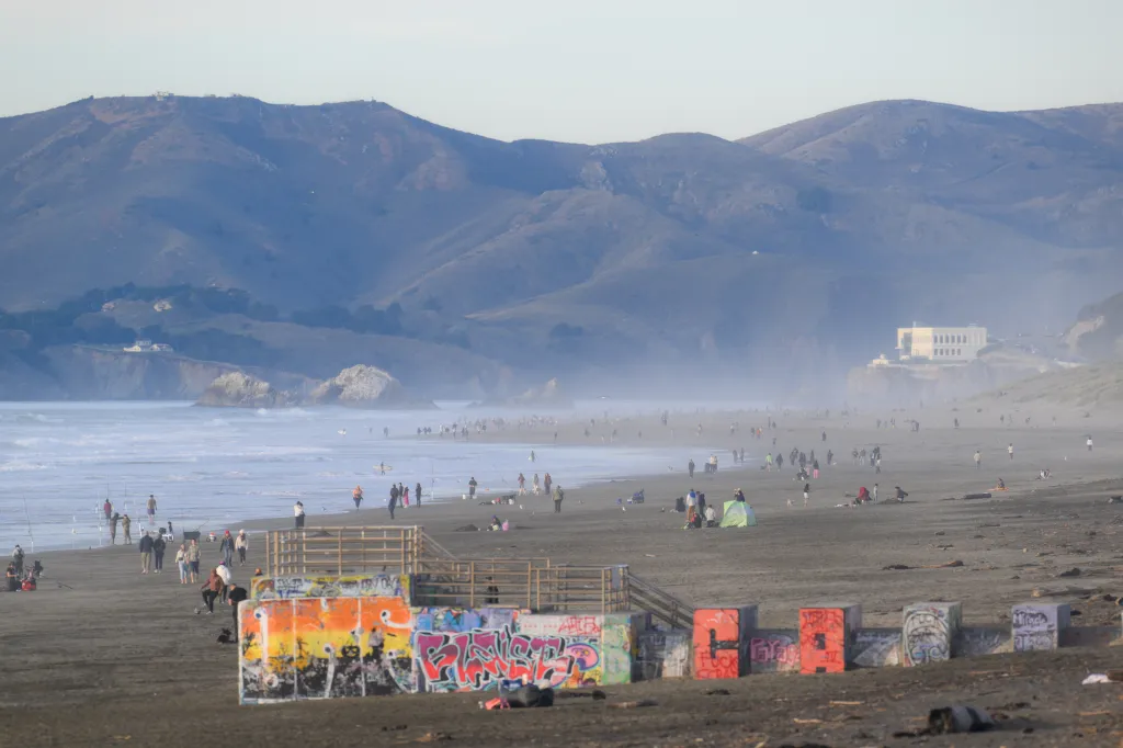 People enjoy the Great Highway Park and Ocean Beach in San Francisco, with mountains in the background.